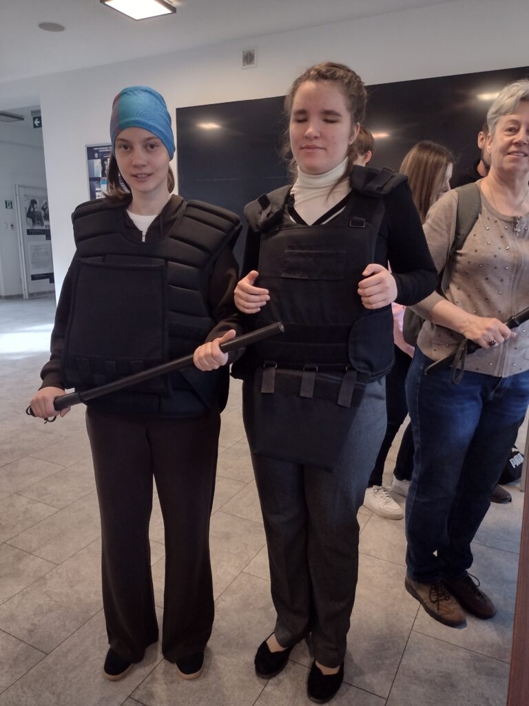 Uczestniczki wycieczki z powagą przymierzają ochronny rynsztunek – kamizelki ochronne, trzymając w rękach pałki, i sprawdzają, jak to jest być „gotowym do akcji”.