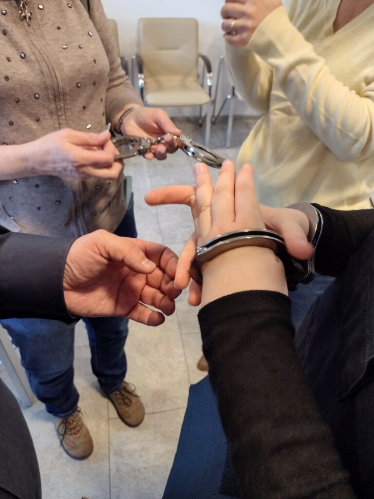 Uczestnicy wycieczki w Wydziale Edukacji Historycznej GKGP przyglądają się budowie kajdanek, a jedna z osób ma okazję sprawdzić, jak działają one w praktyce.