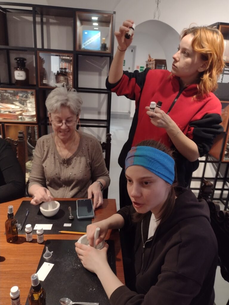 Pod czujnym okiem instruktorki, uczestniczki warsztatów w Muzeum Farmacji starannie ucierają składniki i analizują aromaty olejków, próbując skomponować swoją idealną wodę zapachową.