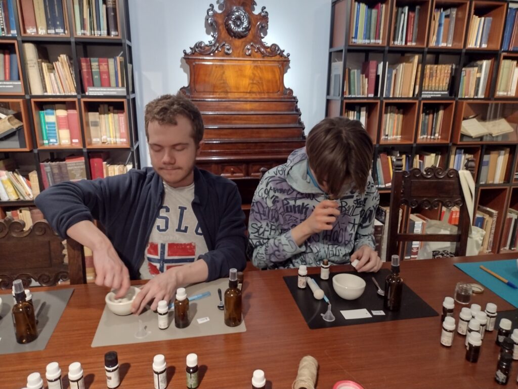 Uczestnicy warsztatów w Muzeum Farmacji z wielkim skupieniem oddają się „sztuce wyboru”, ucierając składniki w moździerzach i starannie selekcjonując olejki eteryczne do swoich autorskich wód zapachowych.