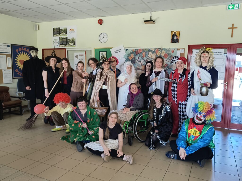 Zdjęcie przedstawia liczną grupę uczniów i nauczycieli w różnorodnych, pomysłowych kostiumach postaci literackich, pozujących wspólnie podczas obchodów Światowego Dnia Książki w szkole „Jabłonki”.