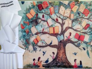 Zdjęcie przedstawia artystyczną dekorację szkolną przygotowaną na teleturniej „Książkoliada jabłonkowa”, ukazującą metaforyczne drzewo z otwartymi książkami zamiast liści, które promuje czytelnictwo wśród społeczności „Jabłonek”.