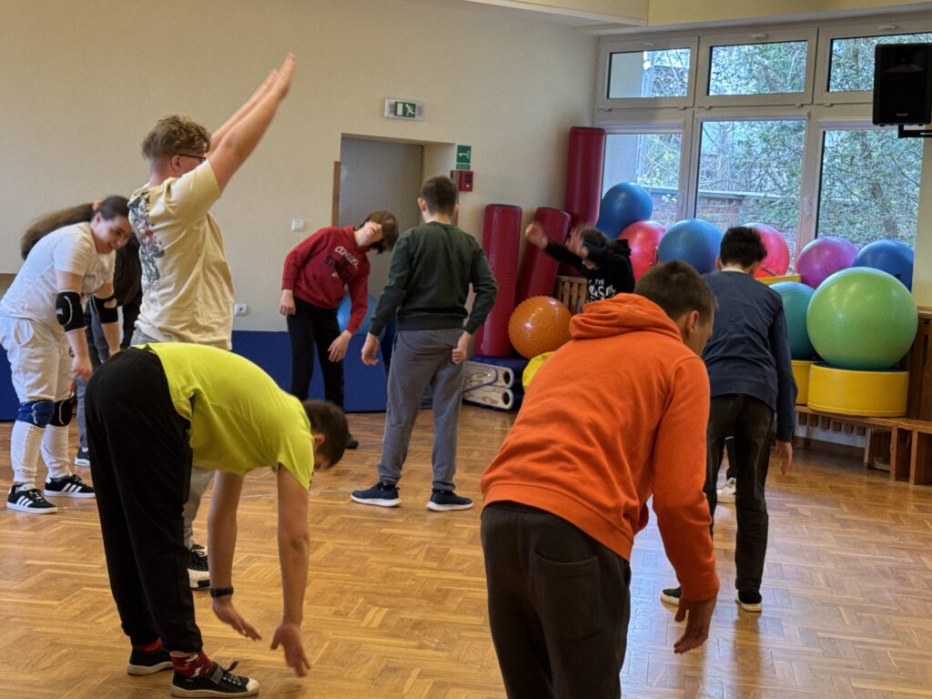 
Uczniowie biorą udział we wspólnej rozgrzewce na sali gimnastycznej, przygotowując swoje ciała do intensywnego wysiłku i sportowej rywalizacji podczas turnieju goalballa.