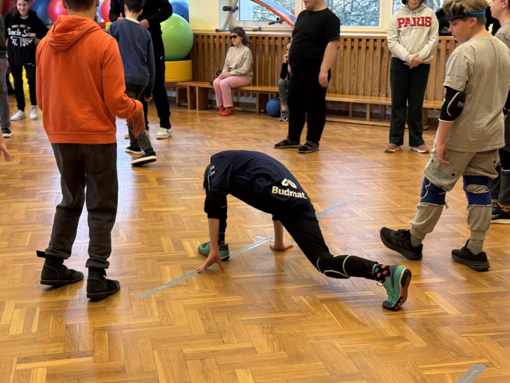 Młody zawodnik w granatowej koszulce wykonuje głęboki wykrok na wyznaczonej linii boiska, intensywnie rozgrzewając się przed startem w turnieju.