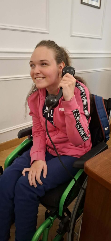 Uśmiechnięta uczestniczka wycieczki, podczas wizyty w Wydziale Edukacji Historycznej GKGP, ma okazję przetestować dawne wyposażenie policyjne, trzymając w ręku słuchawkę zabytkowego telefonu.