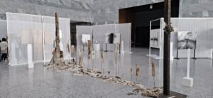 Zdjęcie przedstawia fragment wystawy czasowej „Gero Hellmuth. Przeciw zapomnieniu” w nowoczesnych wnętrzach Muzeum Historii Polski, gdzie surowe, wielkoformatowe obrazy i instalacje z użyciem drewna oraz tkanin tworzą przestrzeń skłaniającą zwiedzających do refleksji nad historią.