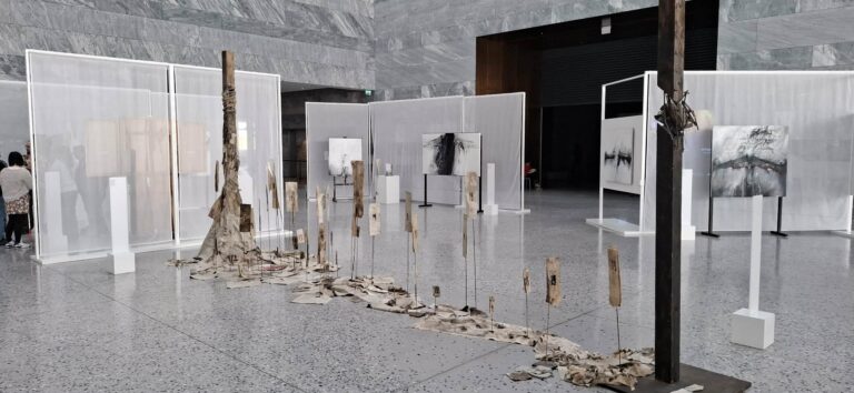 Zdjęcie przedstawia fragment wystawy czasowej „Gero Hellmuth. Przeciw zapomnieniu” w nowoczesnych wnętrzach Muzeum Historii Polski, gdzie surowe, wielkoformatowe obrazy i instalacje z użyciem drewna oraz tkanin tworzą przestrzeń skłaniającą zwiedzających do refleksji nad historią.