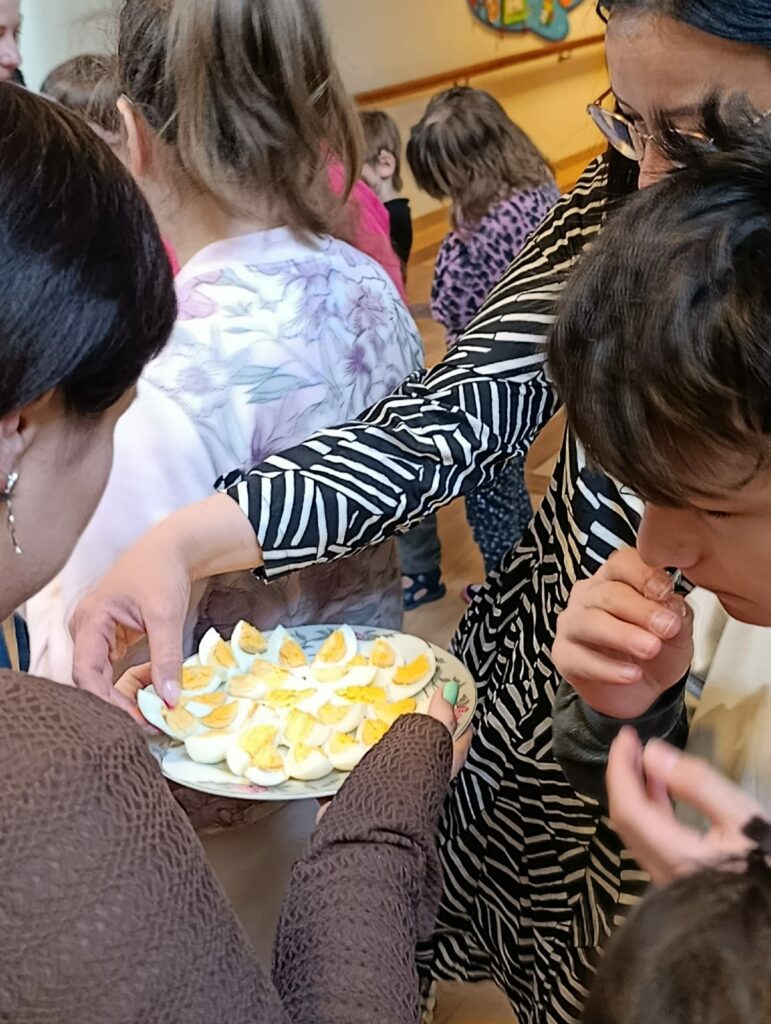 Na pierwszym planie znajduje się talerz z jajkami, w tle- uczniowie i nauczyciele