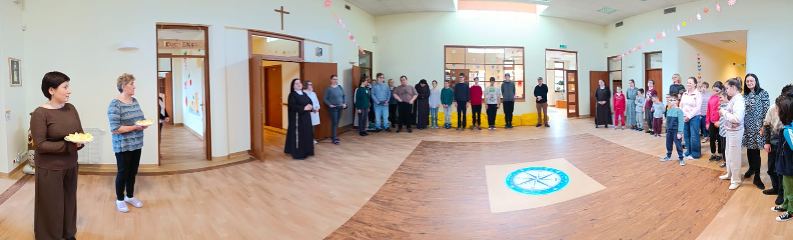 Uczniowie i nauczyciele stojący w hallu szkolnym