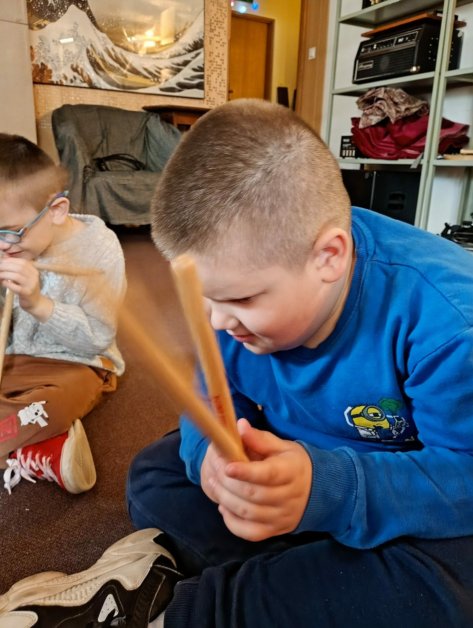 Dwaj siedzący  na podłodze chłopcy  trzymają drewniane pałeczki