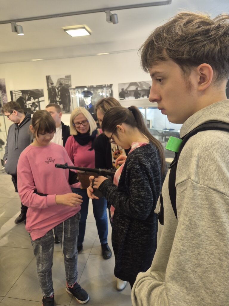 Uczniowie z bliska oglądają i poznają budowę historycznej broni palnej, która stanowiła element dawnego wyposażenia formacji policyjnych.