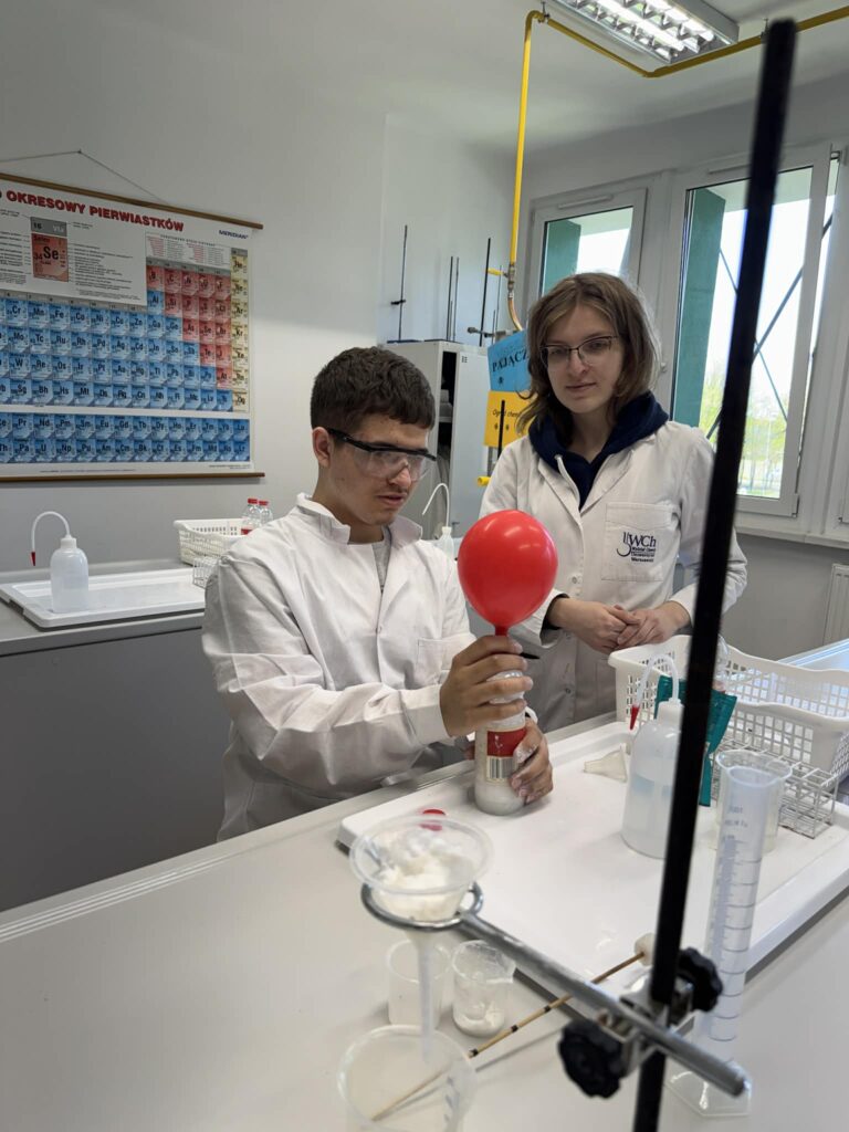 Pod okiem studentki Wydziału Chemii uczniowie z zaangażowaniem przeprowadzali efektowne doświadczenia, takie jak pompowanie balonu gazem powstałym w wyniku reakcji, co pozwoliło im poczuć atmosferę prawdziwej pracy badawczej.
