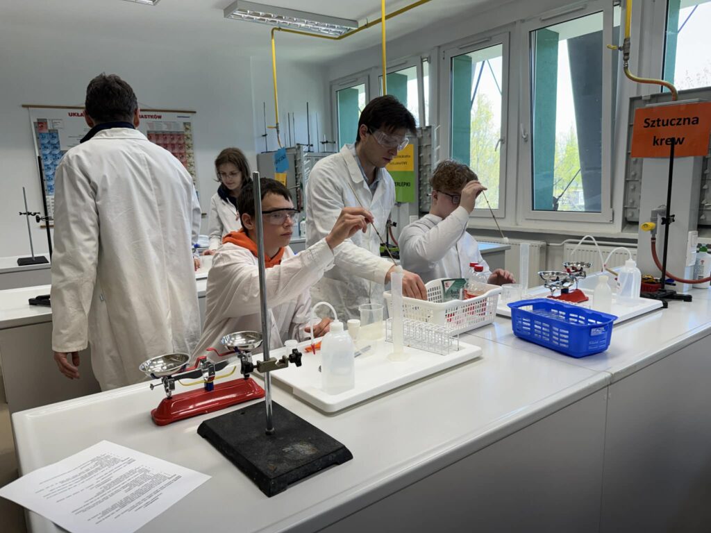W profesjonalnej atmosferze uniwersyteckiego laboratorium uczniowie z ciekawością korzystali ze specjalistycznego sprzętu, takiego jak wagi czy cylindry miarowe, odkrywając pod okiem doświadczonych studentów tajniki pracy naukowej i precyzji wymaganej w badaniach chemicznych.