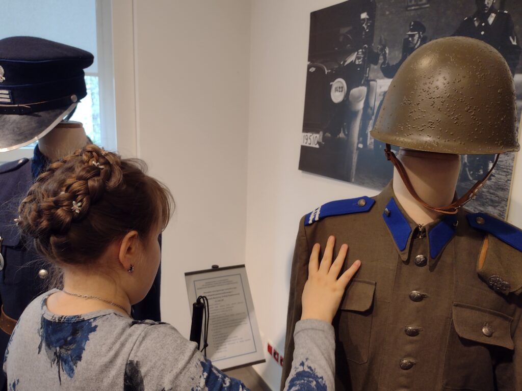 Jedna z uczennic ma możliwość bezpośredniego poznania historii poprzez dotyk, oglądając detale munduru i hełmu Milicji Obywatelskiej eksponowanego na manekinie.