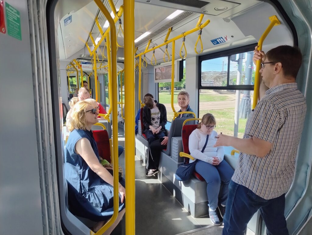 Uczniowie siedzą w tramwaju, przewodnik opowiada