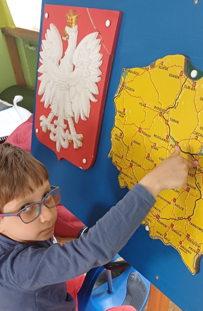 Chłopiec wskazuje miasto na wypukłej mapie Polski.
