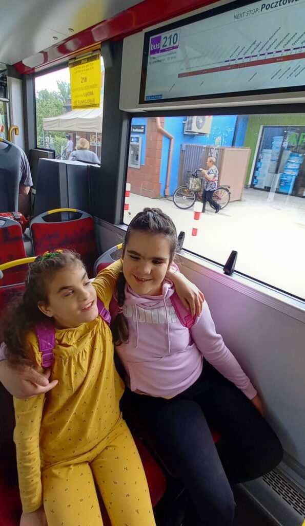 Dwie dziewczynki z gr.1  siedzą obok siebie w  autobusie 210.