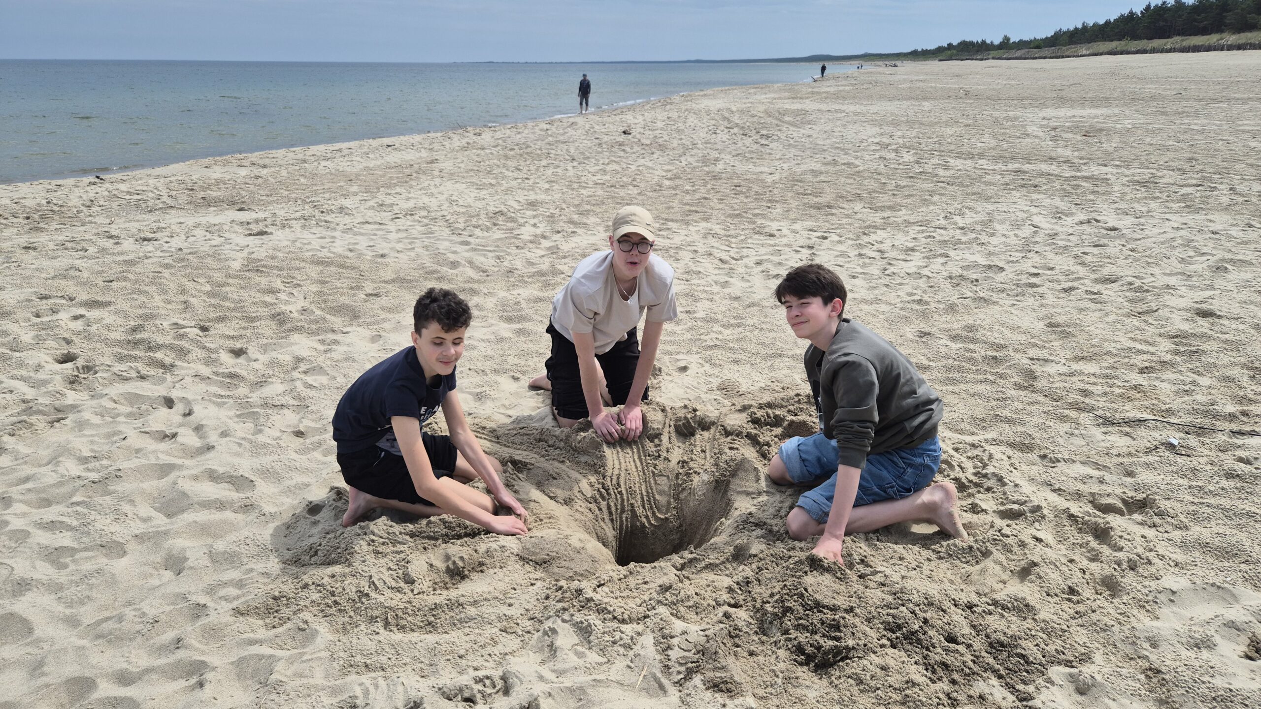 Trzech uczniów kopie dół na plaży