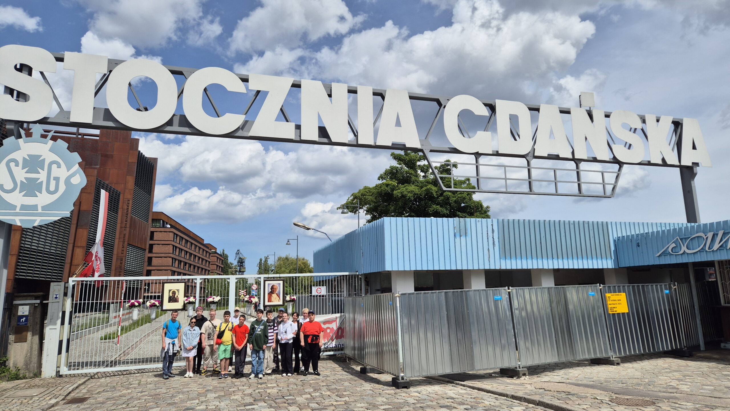 Uczniowie na tle bramy i napisu Stocznia Gdańska