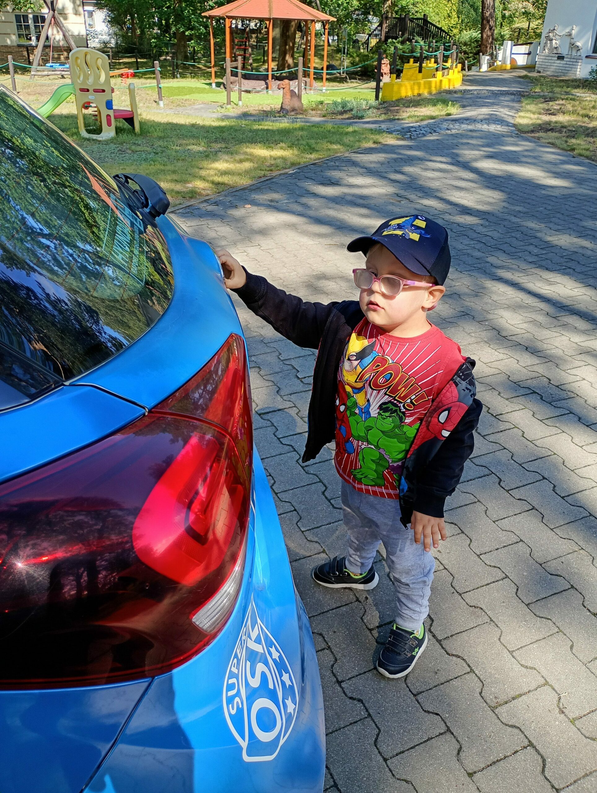 Stojący chłopiec dotyka tylnej części auta.