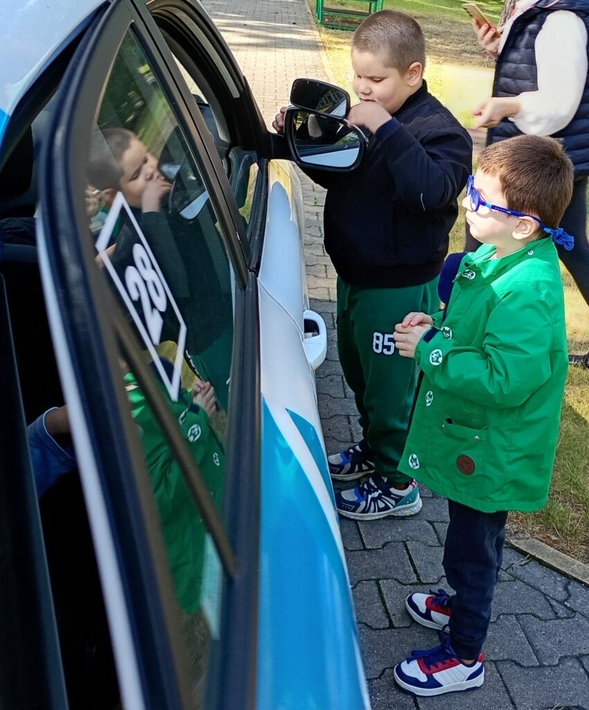 Dwóch chłopców stojących obok auta, jeden z nich dotyka lusterek