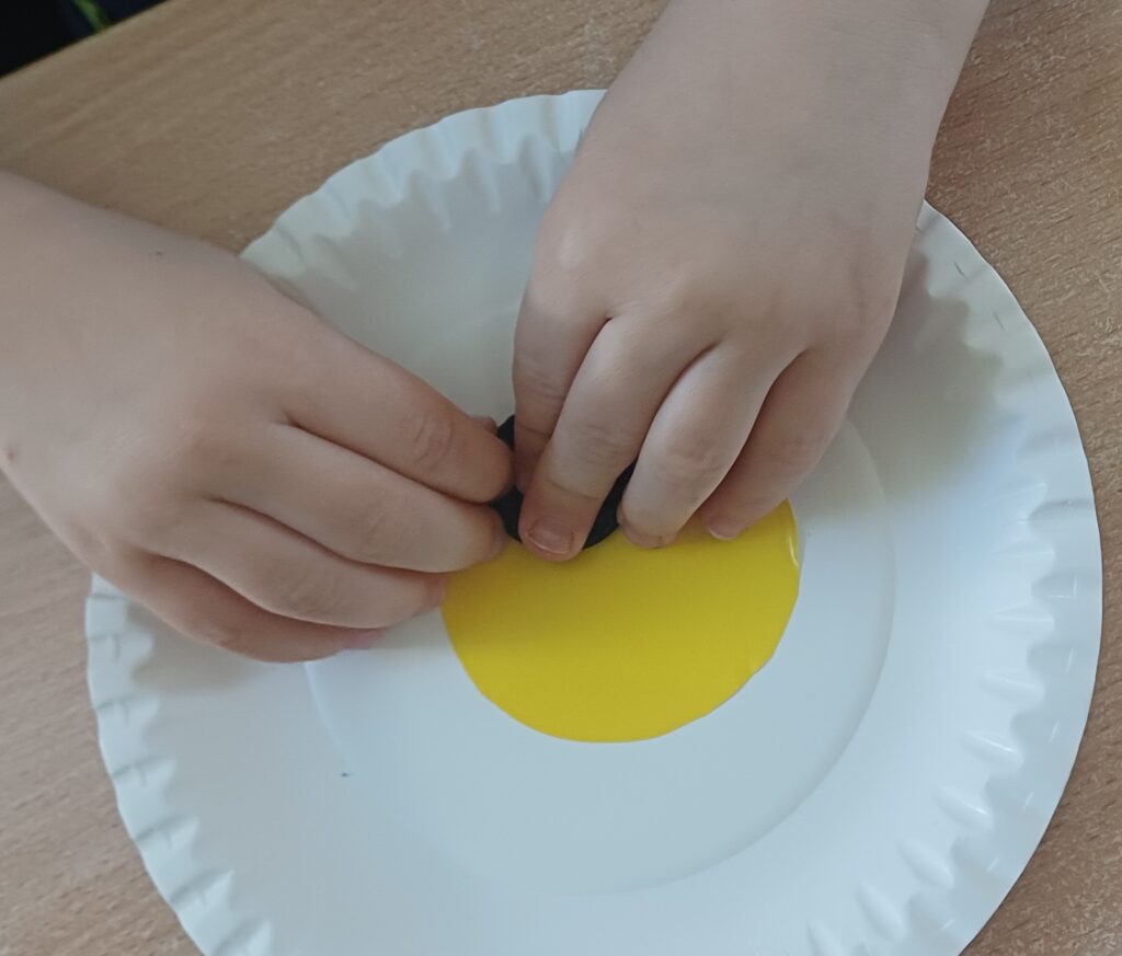 Ręce na papierowym talerzu, na naklejonych kropkach.