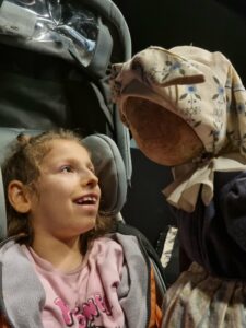 Uśmiechnięta uczennica na wózku nawiązuje bezpośredni kontakt z animowaną lalką teatralną