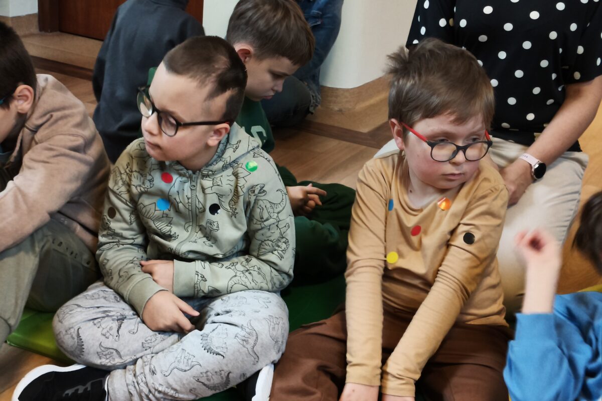 uczniowie z widocznymi na ubraniach kolorowymi kropkami